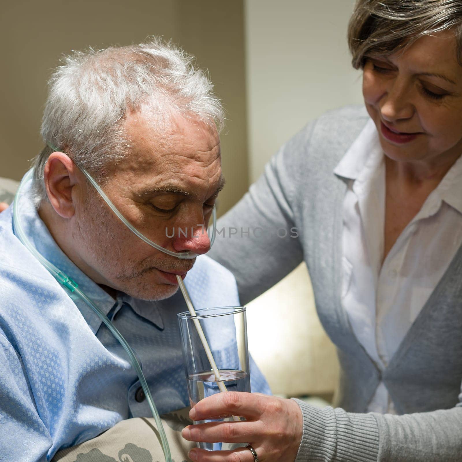 Nurse helping senior sick man with drinking glass of water
