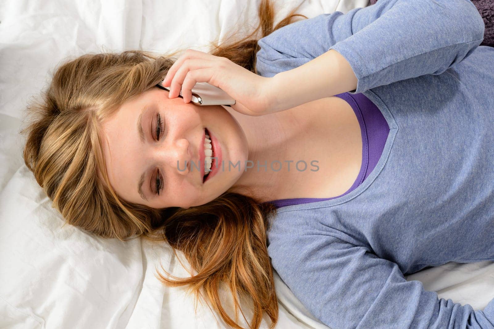 Young girl lying in bed and talking on smart phone
