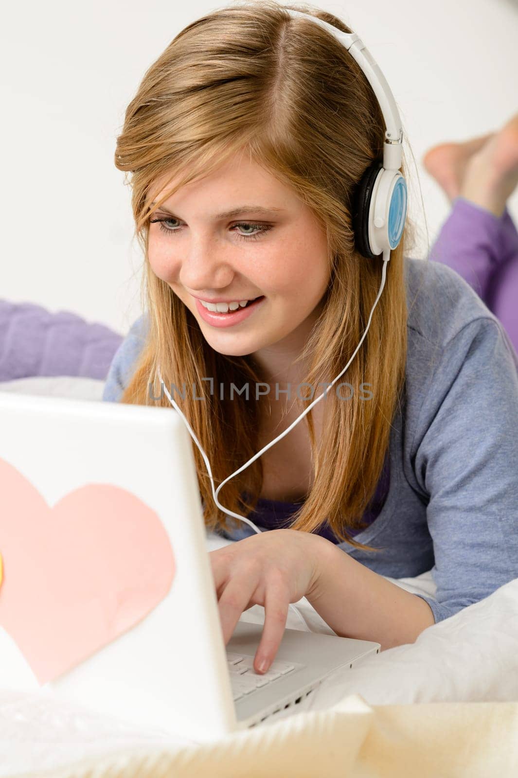 Young teenage girl chatting on laptop and lying on bed