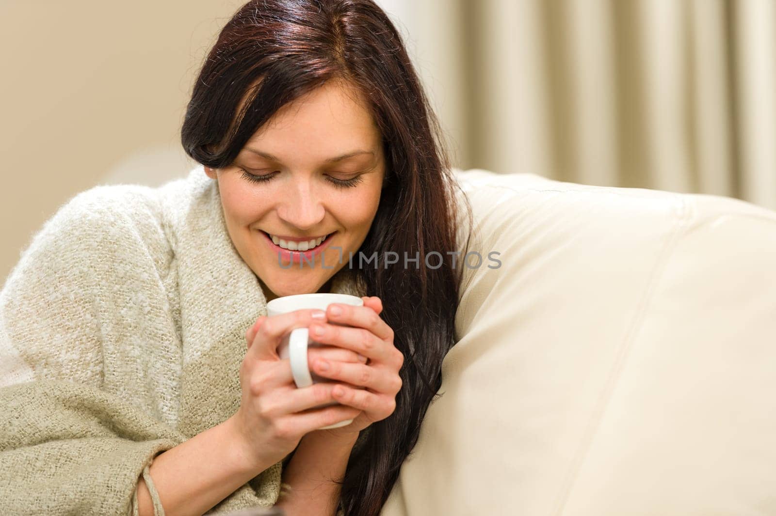 Smiling woman enjoying hot tea sitting on couch