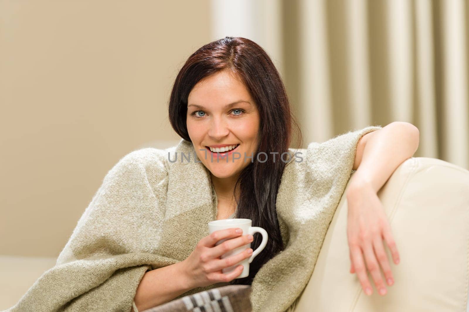 Joyful cozy woman drinking hot drink on sofa