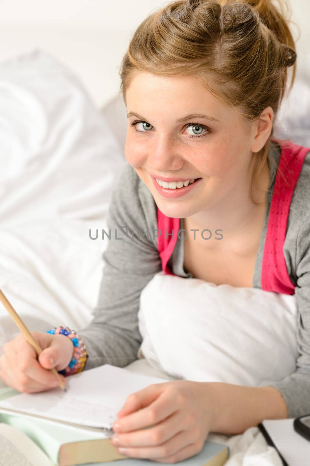 Smiling girl preparing for exams with books lying on bed