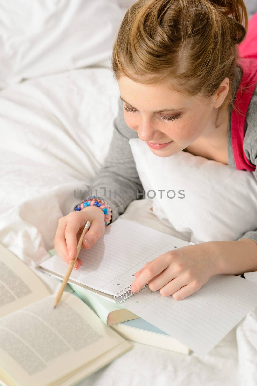 Teenage girl concentrating on studying from book lying on bed