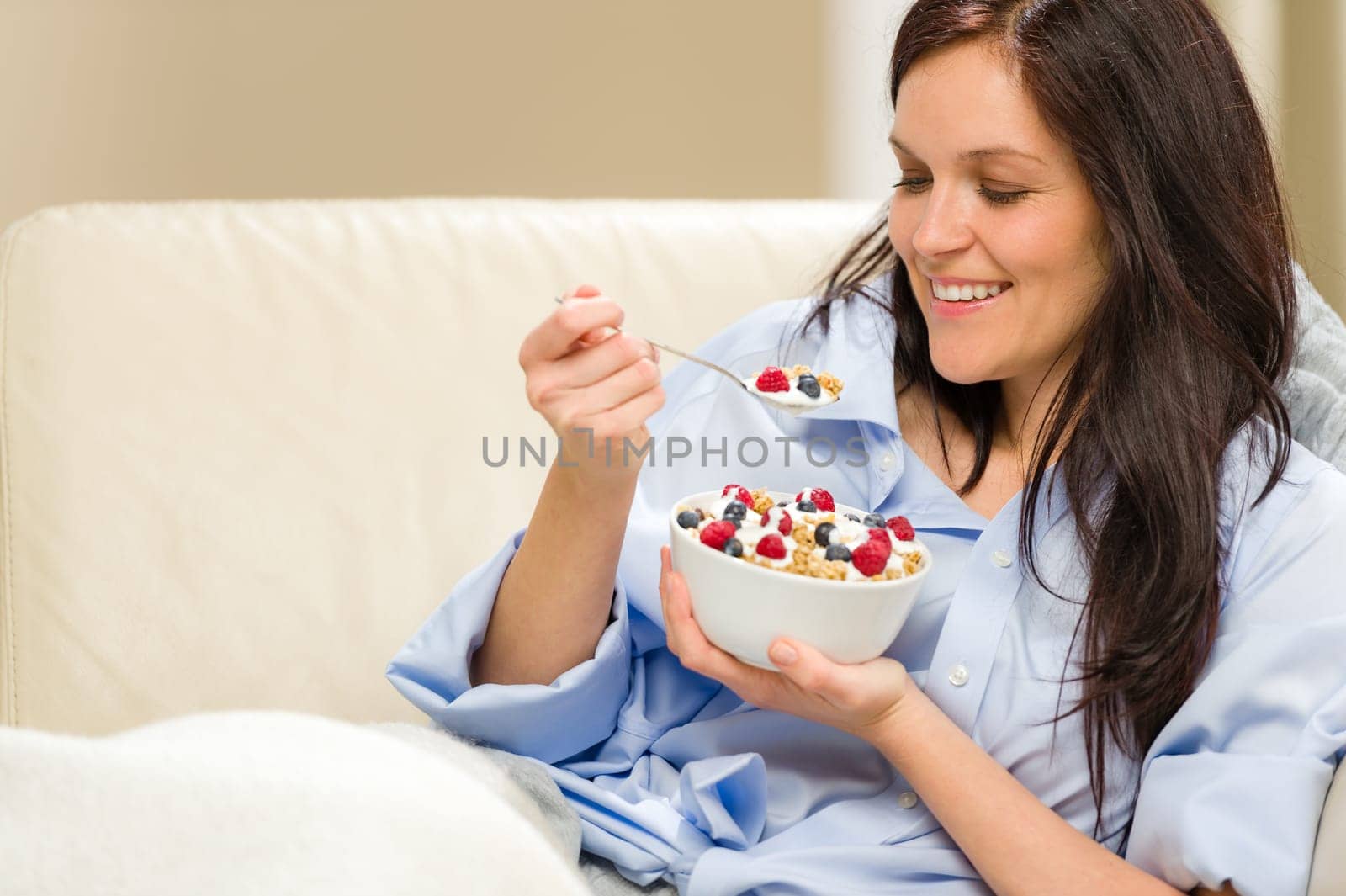 Young smiling woman eating healthy cereal lying on couch