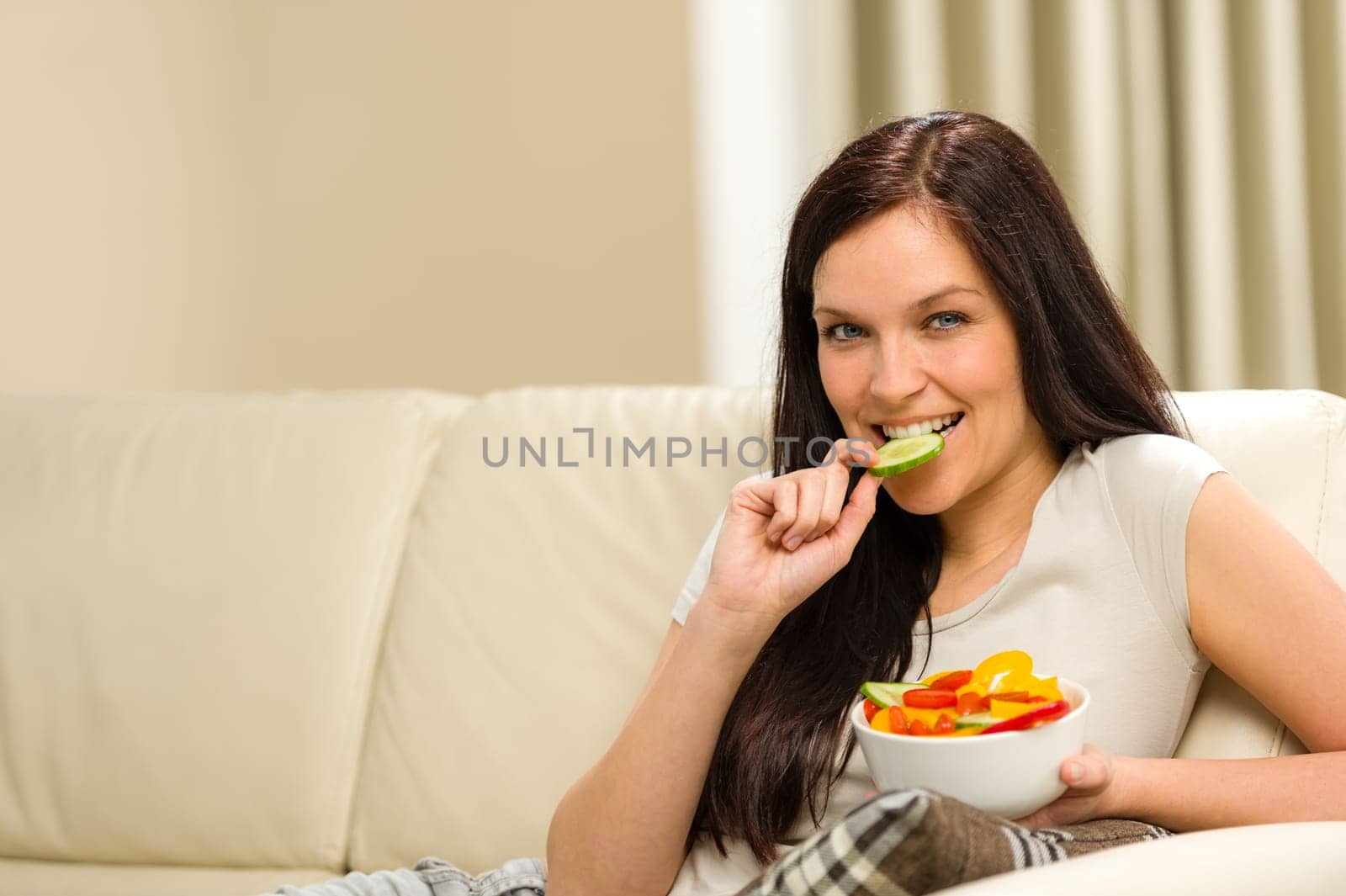Woman sitting on sofa eating colorful mixed salad
