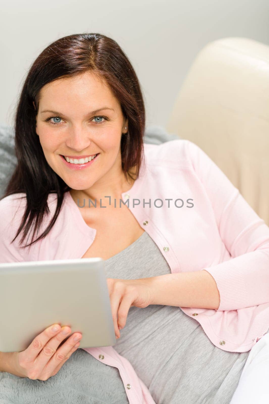 Beautiful joyful woman holding digital tablet lying on couch