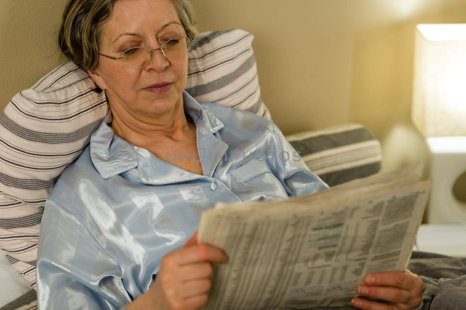 Retired woman reading newspaper before sleeping in bedroom