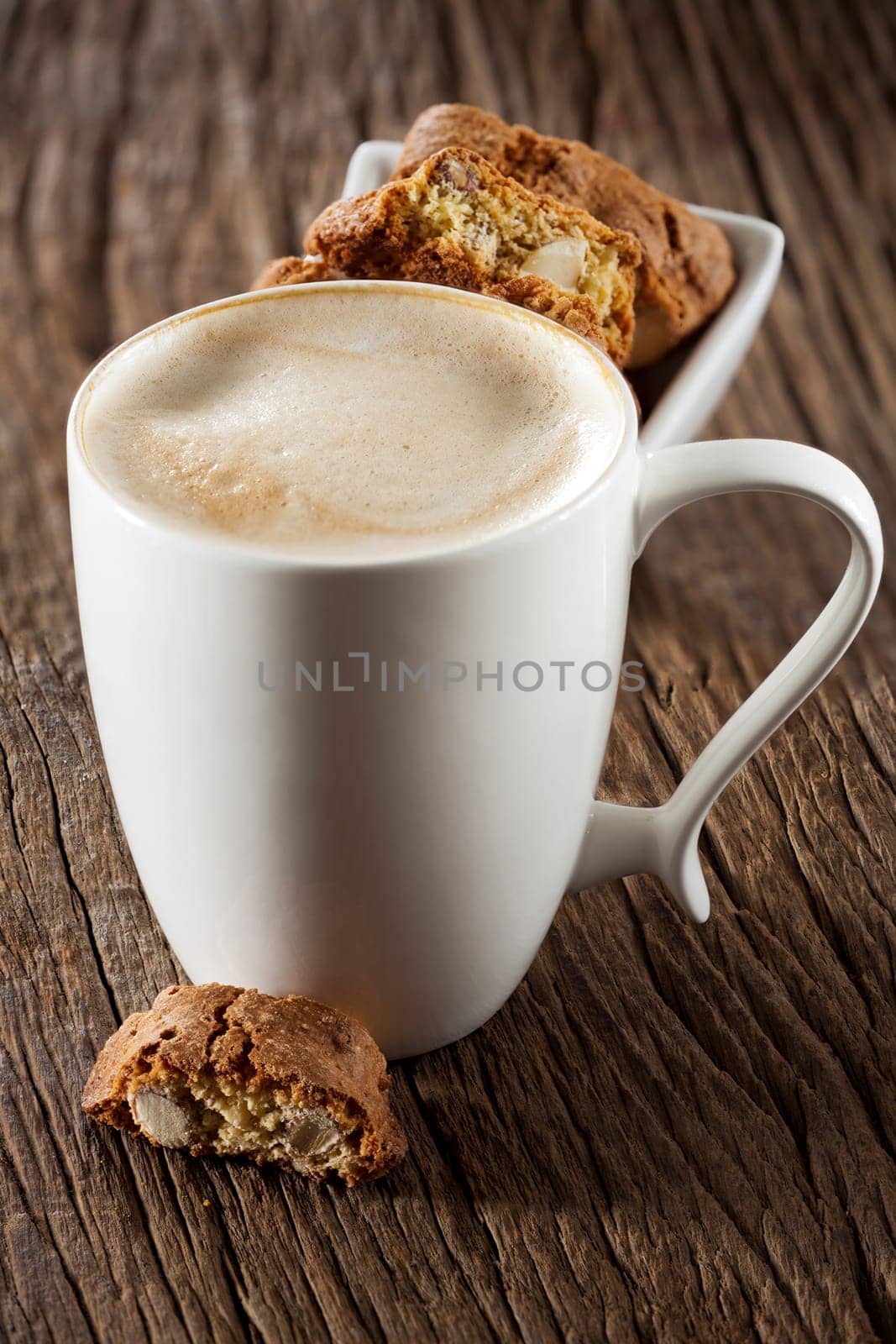 A cup of cappuccino and fine cantuccini pastries on a wooden surface