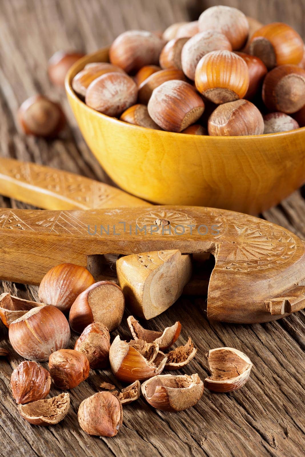 Whole hazelnuts in a wooden bowl and cracked hazelnuts with a wooden nutcracker on a rustic wooden surface