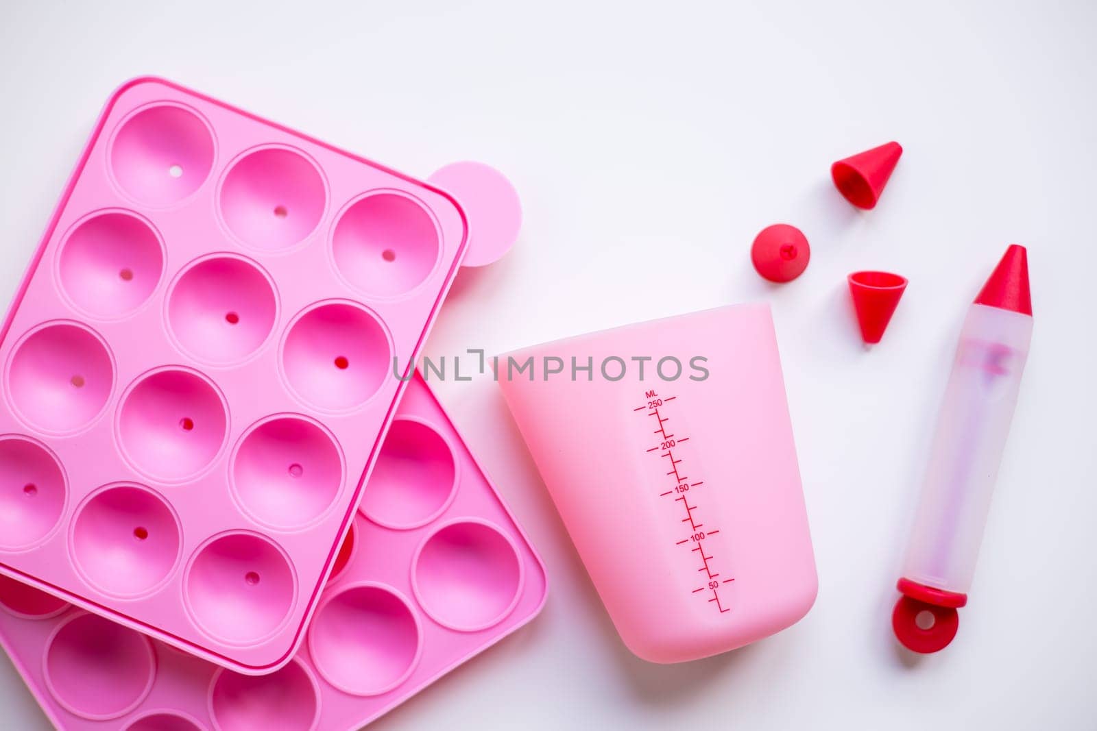Pink baking utensils set with silicone molds and measuring cup on white background.
