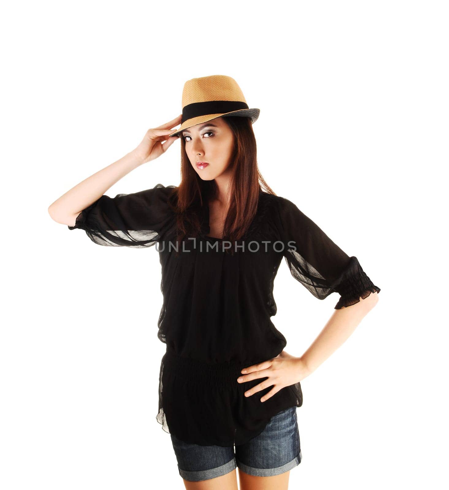 A tall young Chinese woman standing for white background in a black blouse and jeans shorts with a straw hat on her head
