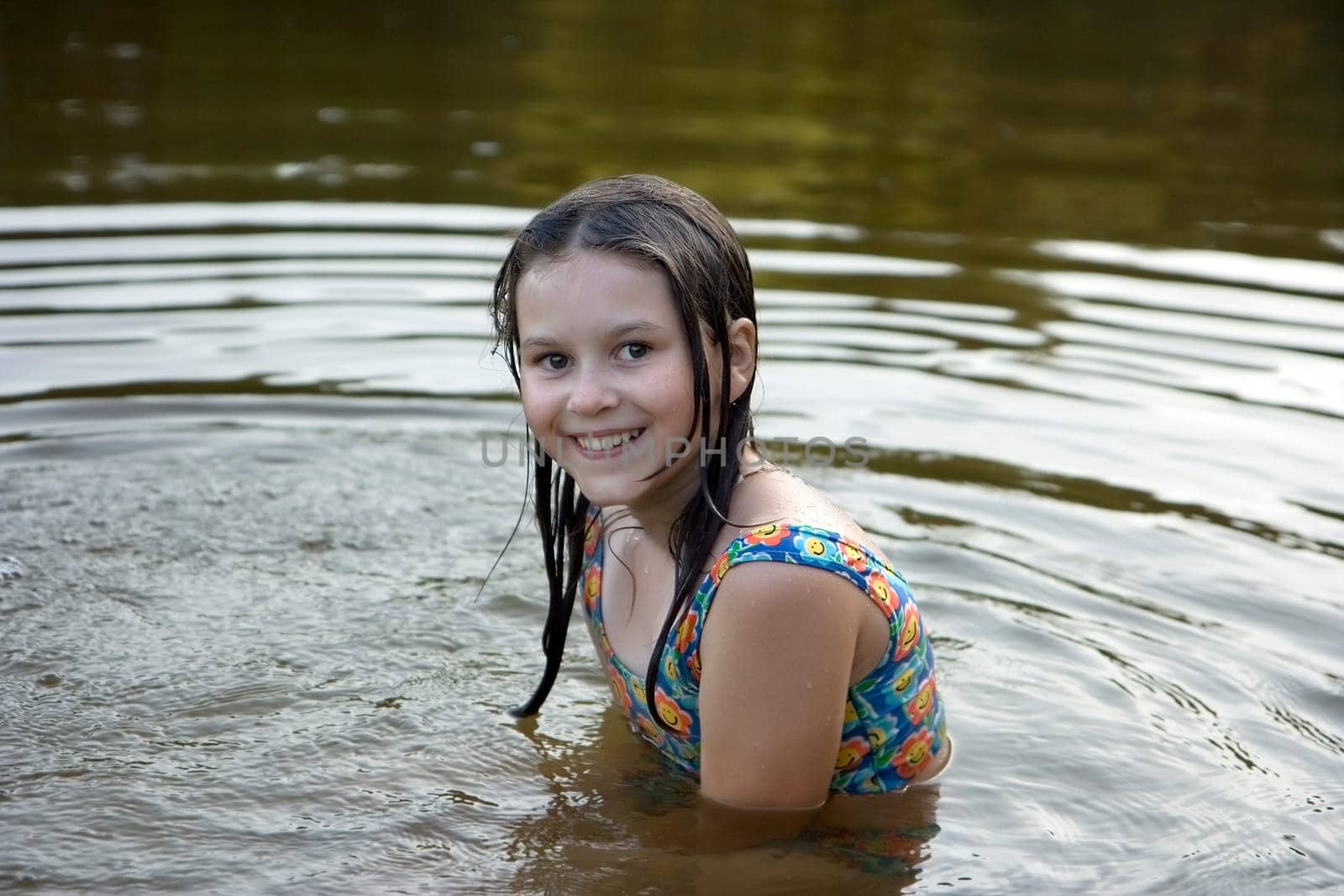 The girl with wet hair sits on a belt in water and smiles