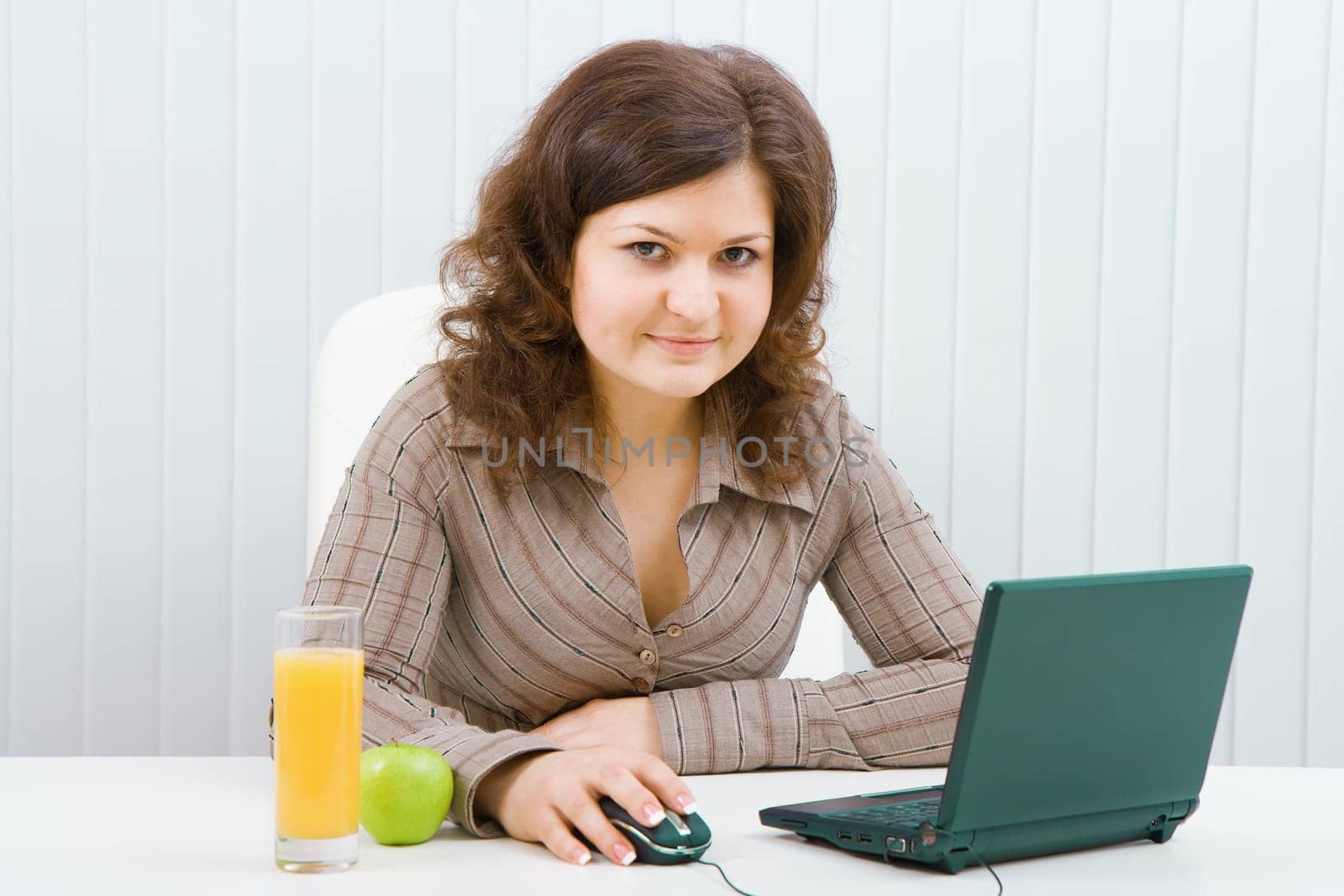 Young smiling woman with a laptop and juice sits in the office