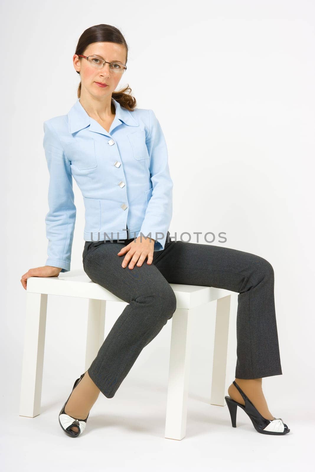 skinny girl with glasses and a suit sitting on a white stool