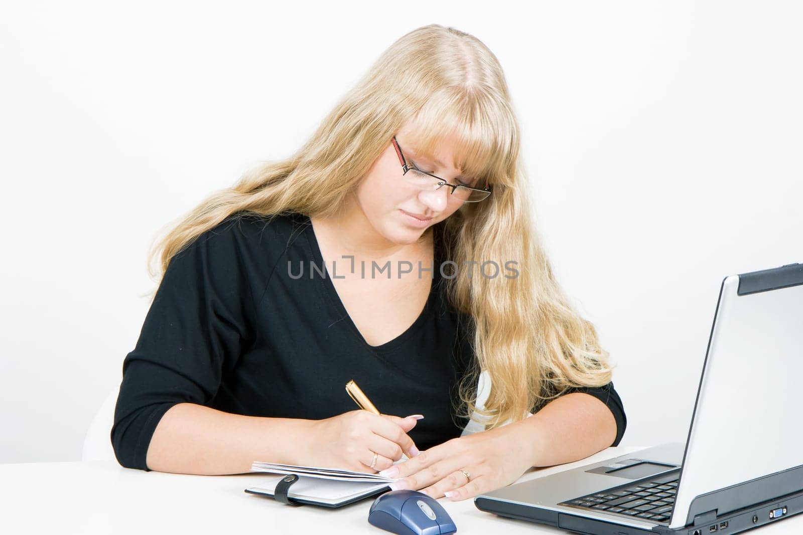 blonde girl with a laptop writes in a notebook