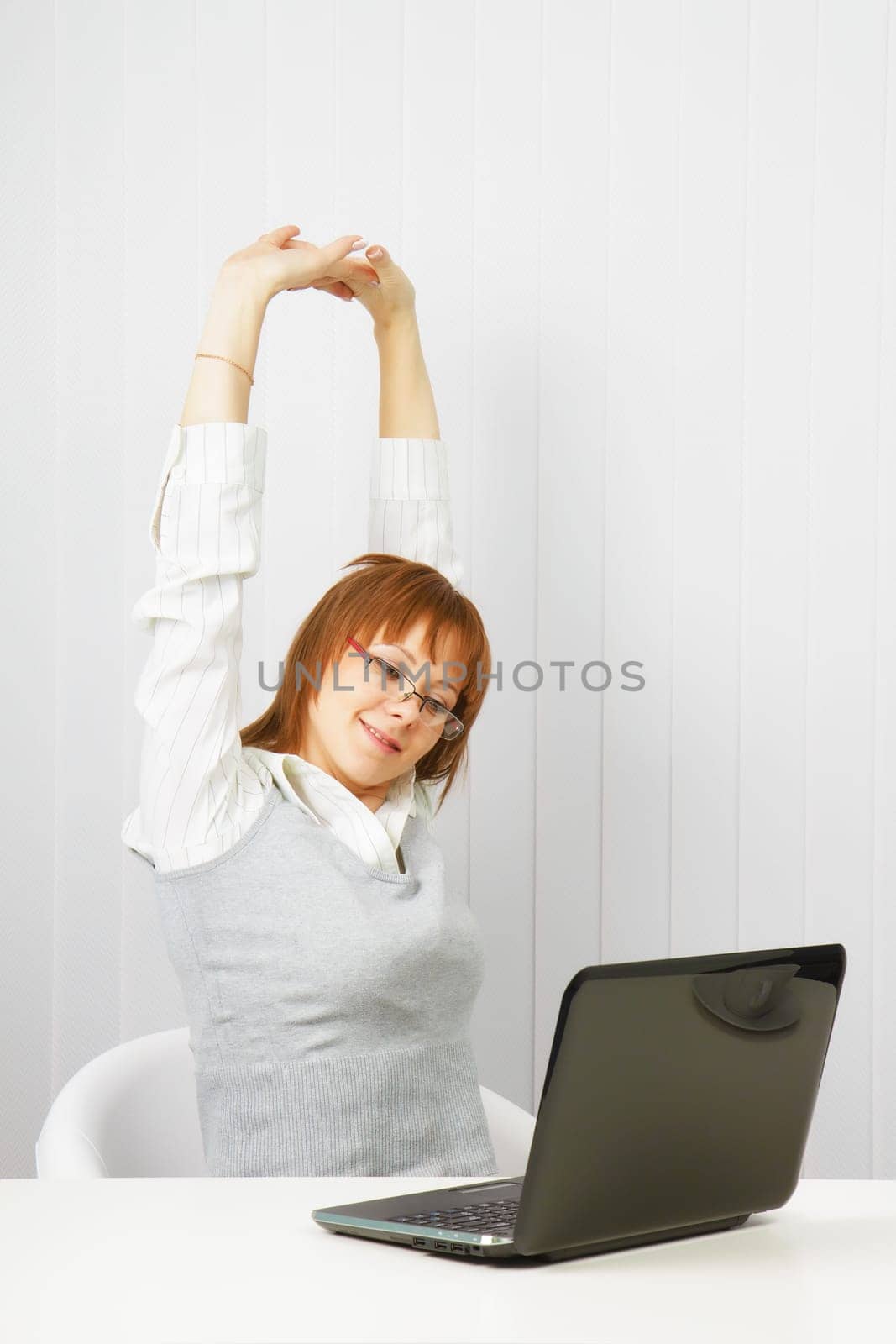 tired girl with a laptop stretches in the workplace