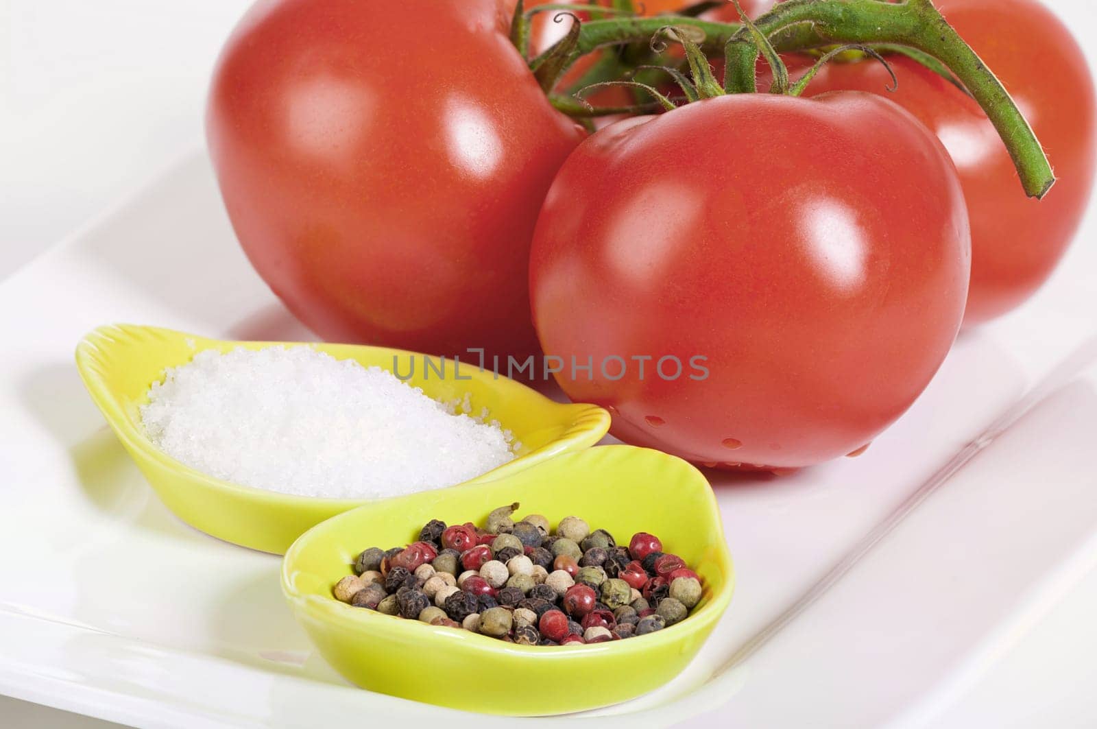 Fresh vine tomatoes with a bowl of fleur de sel and a bowl of peppercorns