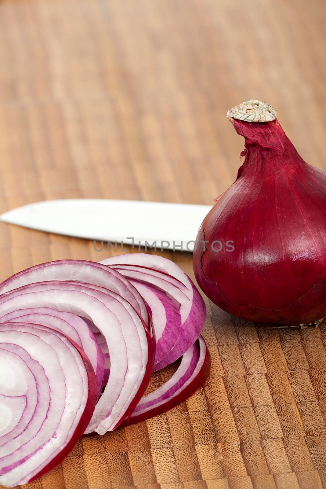 A whole red onion and onion rings with a knife on a cutting board