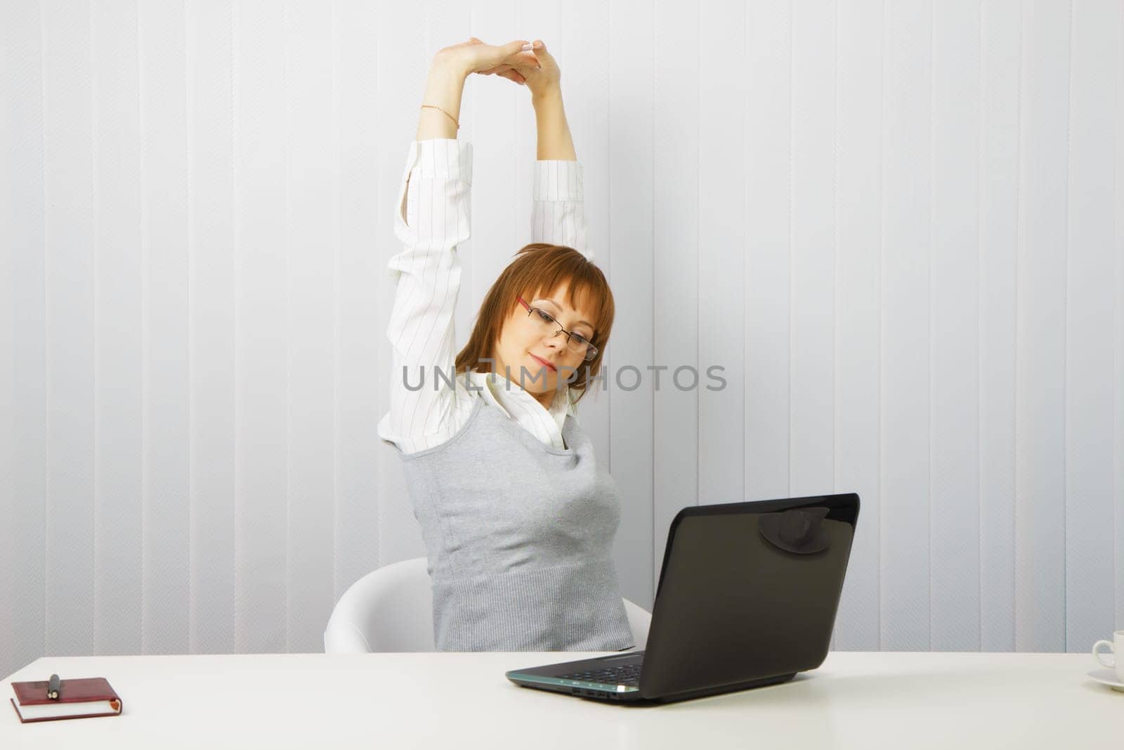 tired girl with a laptop stretches in the workplace