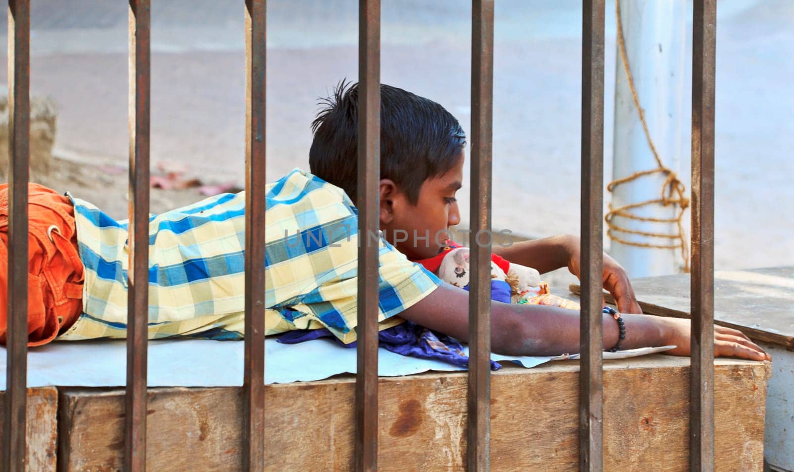 horizontal urban color landscape of a teenage boy laying on his stomach on a makeshift bed by roadside railings pondering daydreaming near his family possessions