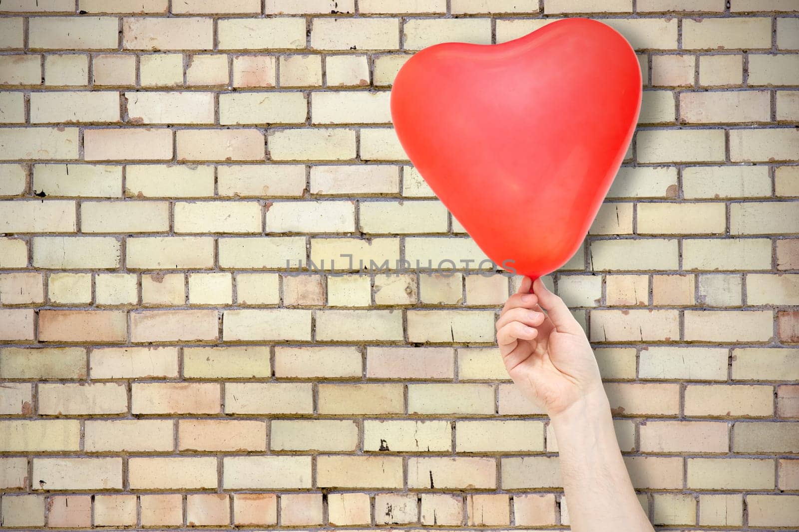 Hand with red balloon against brick wall background