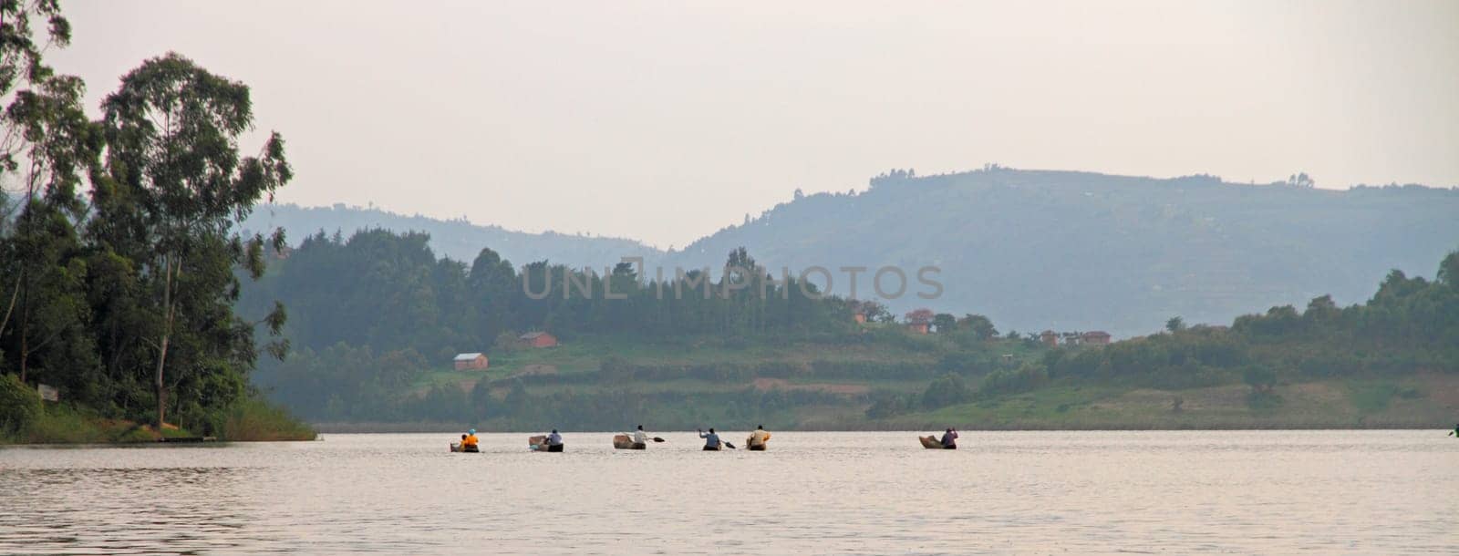 LAKE BUNYONI, UGANDA - CIRCA SEPTEMBER 2012- A group of people paddle their dugout canoes to get across the waters of Lake Bunyoni in Uganda, Africa.