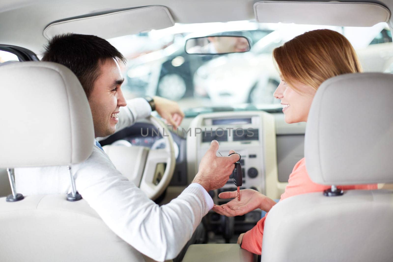 Rear view of pretty woman looking at salesman while taking key from new car