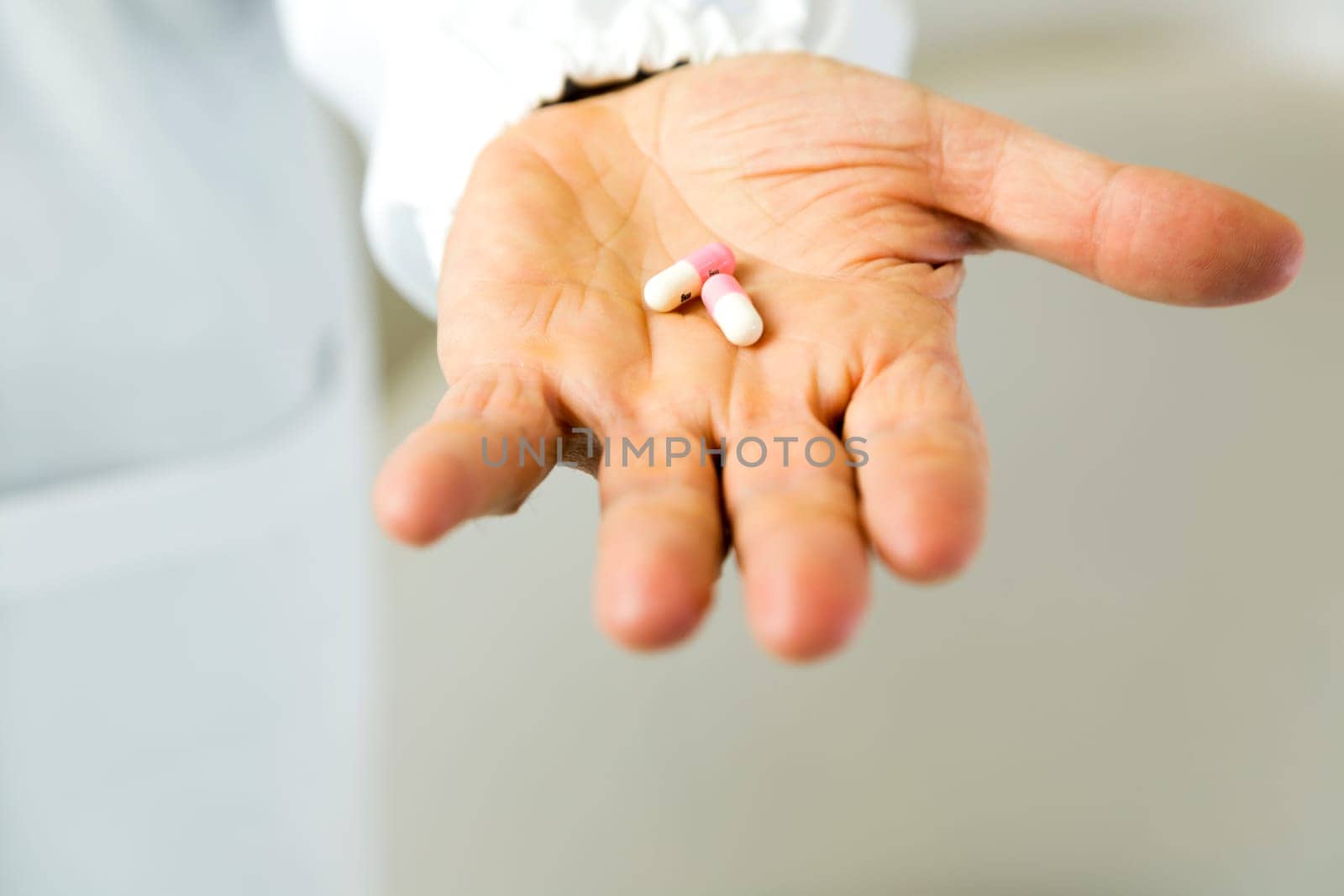 Doctor holding white and pink pills against anxiety on light gray background