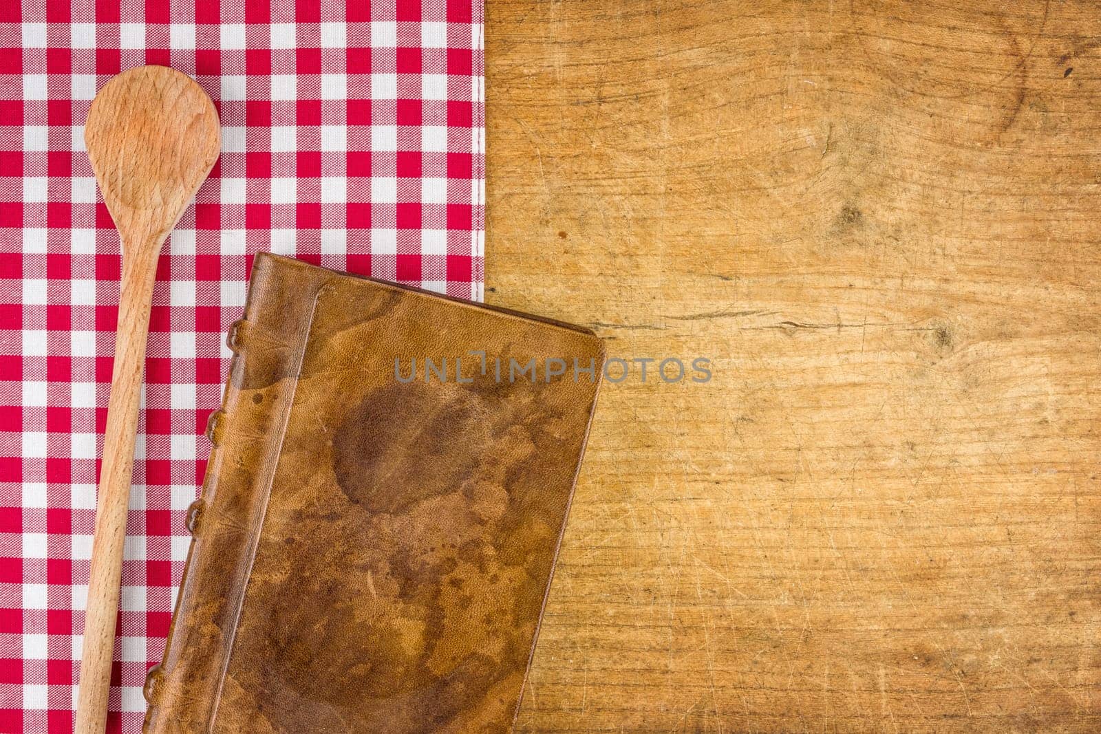 Wooden spoon and book on a wooden board with checkered tablecloth