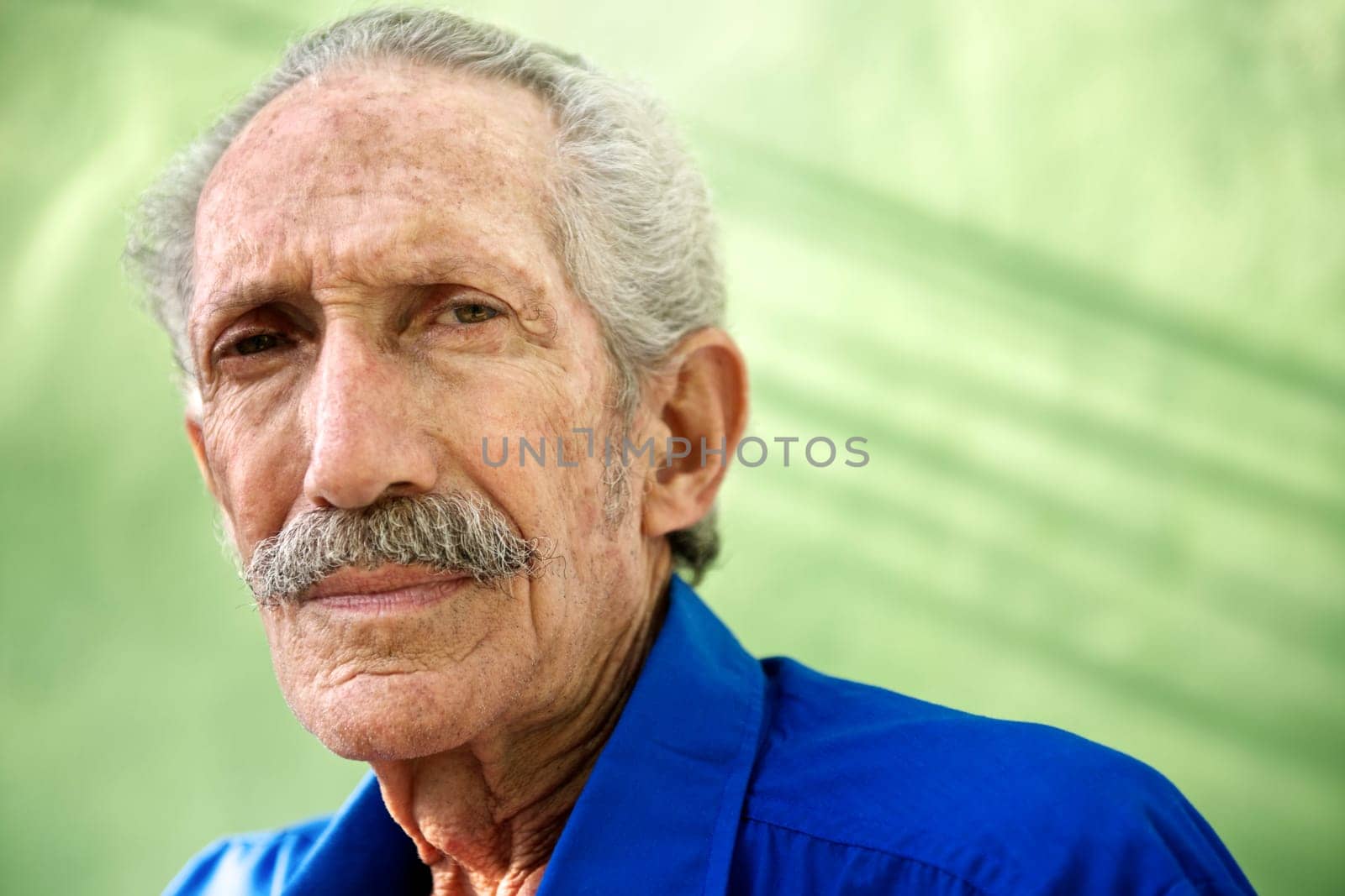 Elderly people and emotions, portrait of serious senior caucasian man looking at camera against green wall