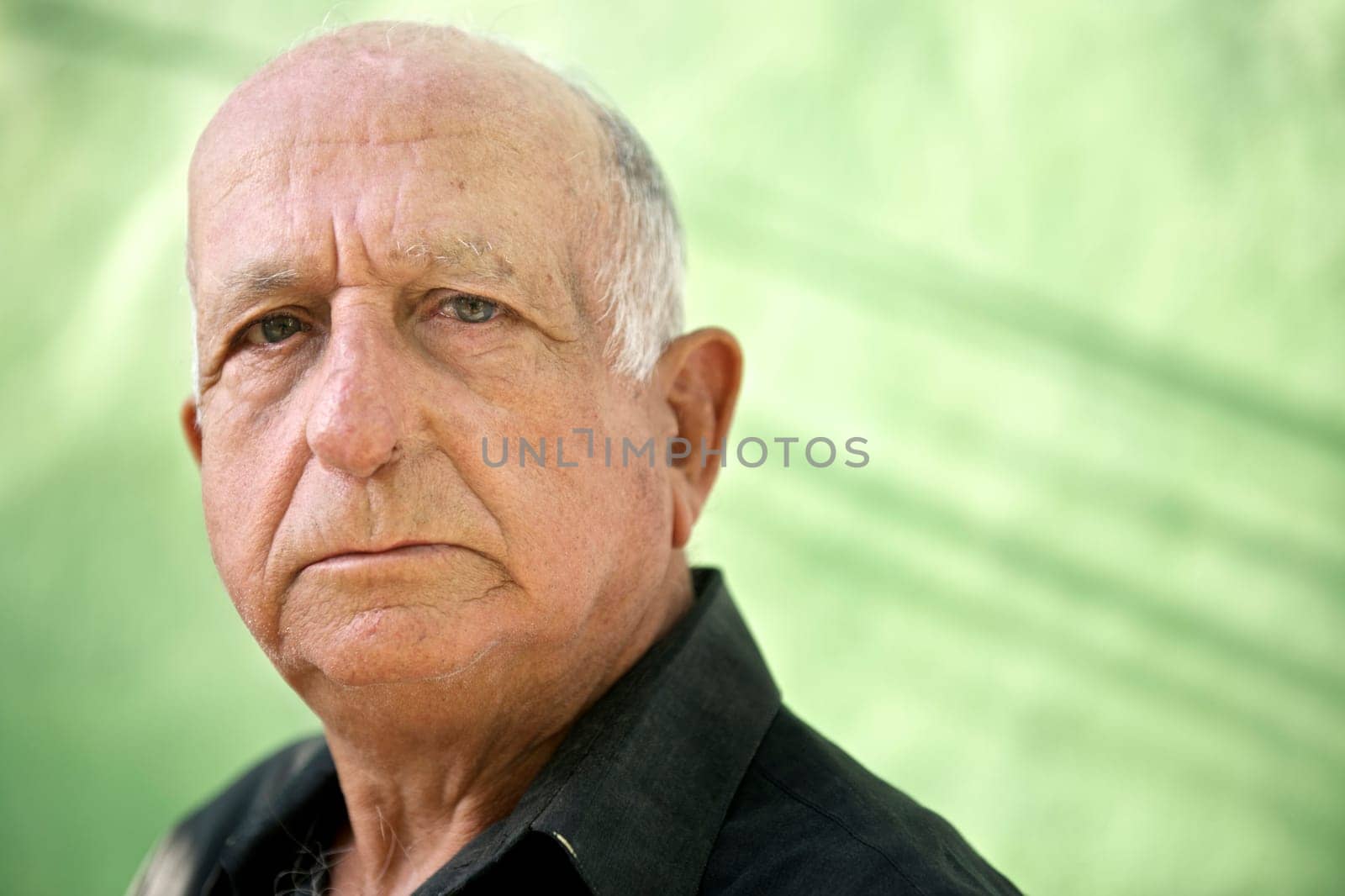Elderly people and emotions, portrait of serious senior caucasian man looking at camera against green wall