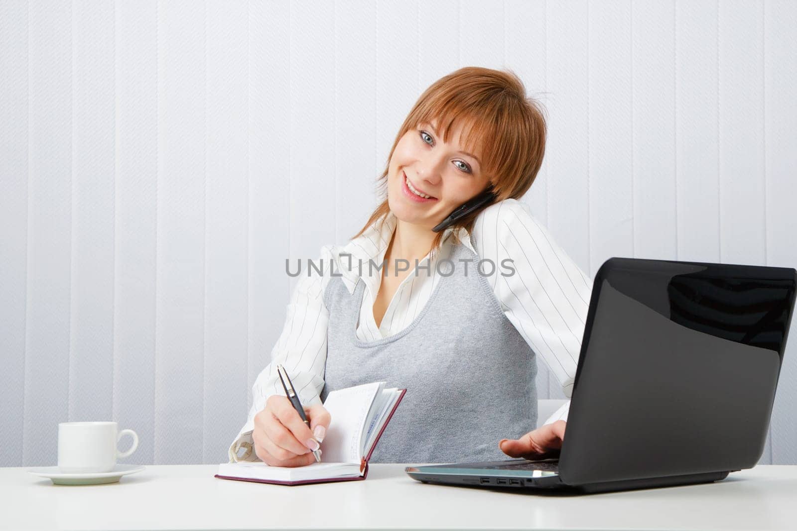 Attractive happy girl talking on the phone and writes simultaneously