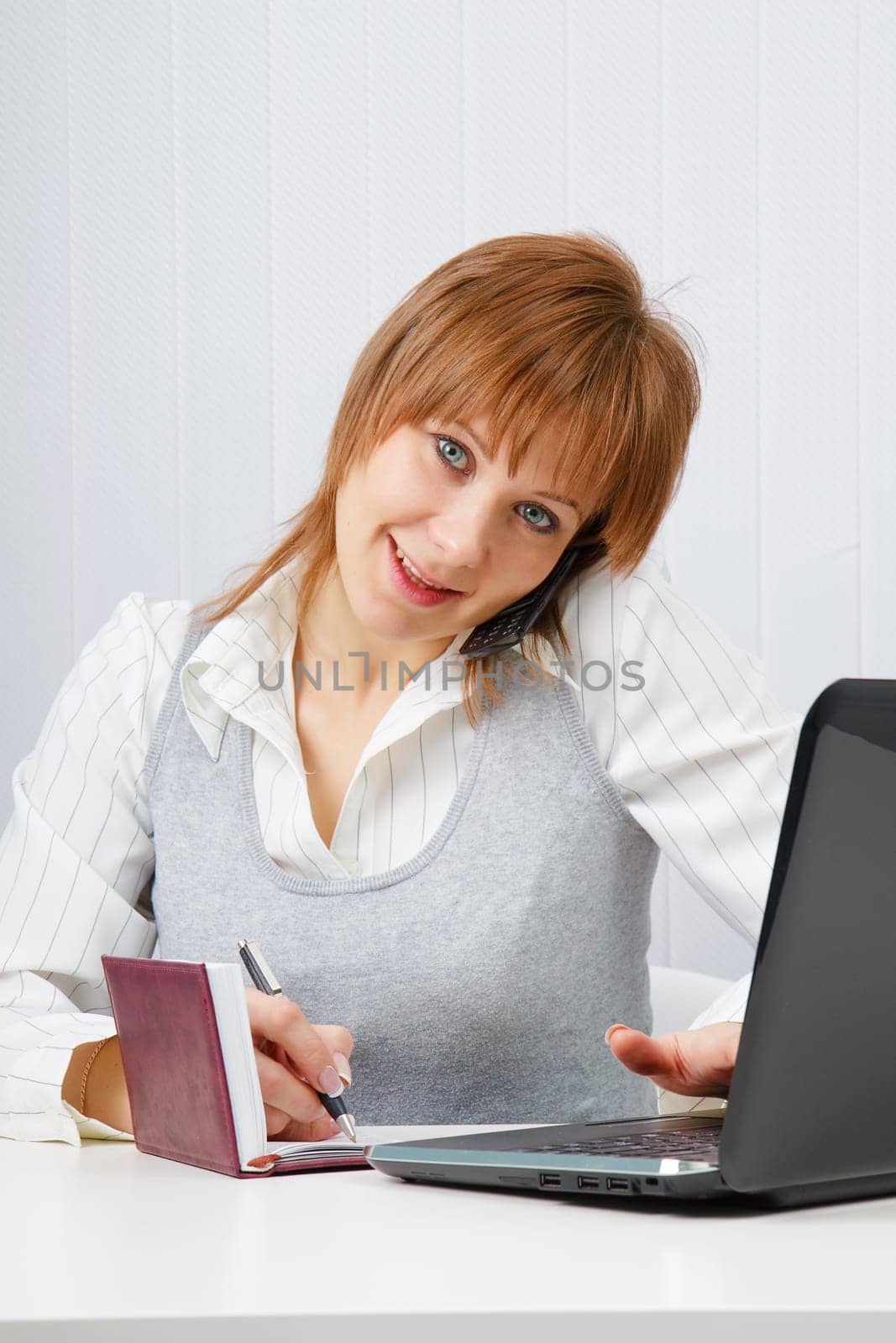Attractive happy girl talking on the phone and writes simultaneously