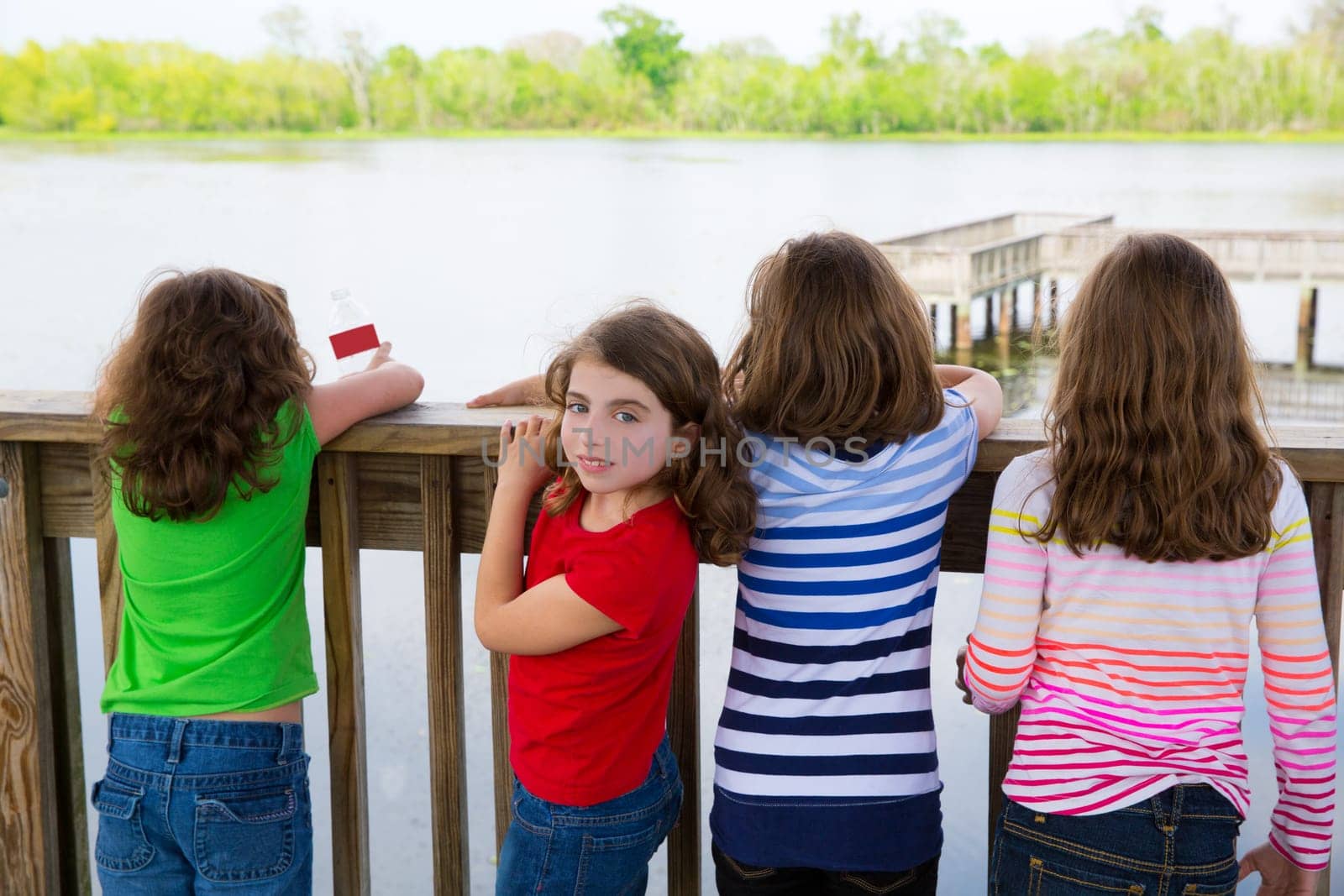 Children girls rear view looking at lake on railing and one looking behind