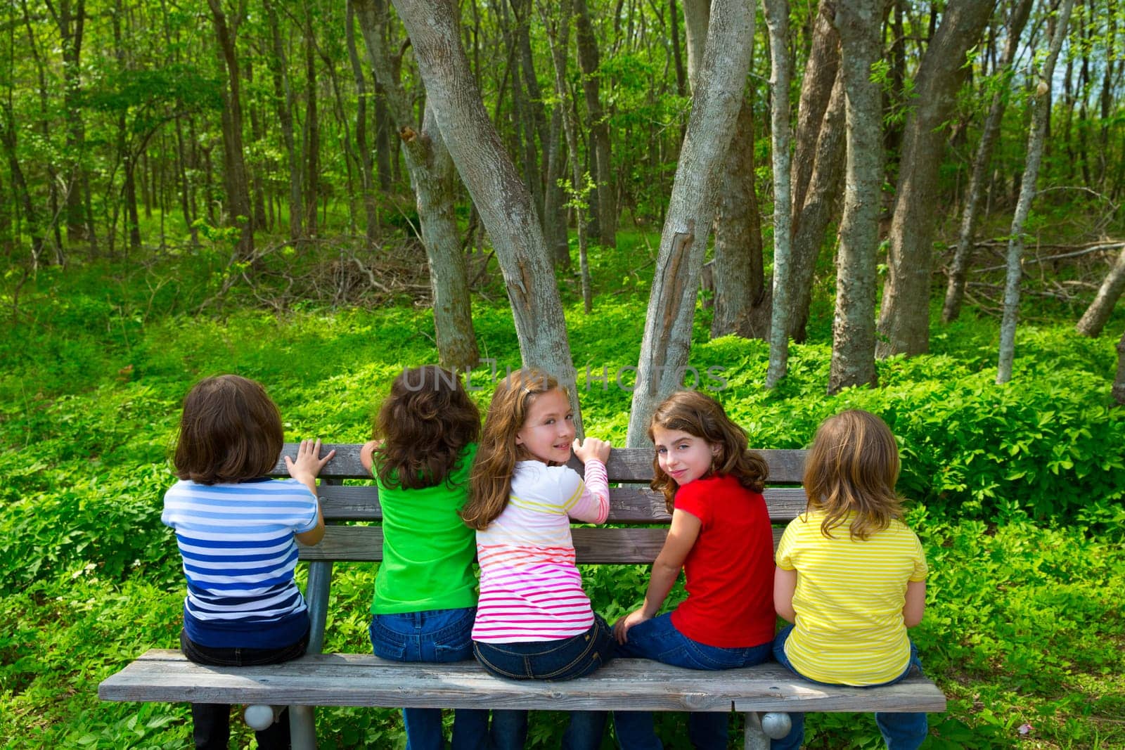 Children sister and friend girls sitting on park bench looking at forest and smiling