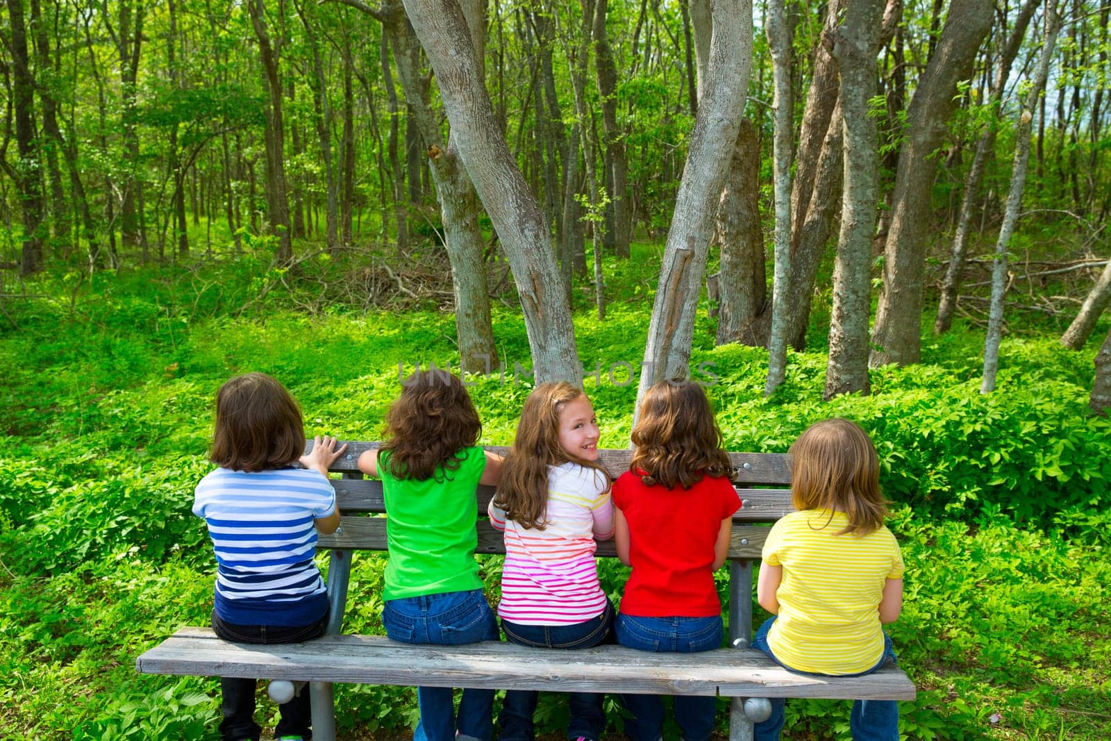 Children sister and friend girls sitting on park bench looking at forest and smiling