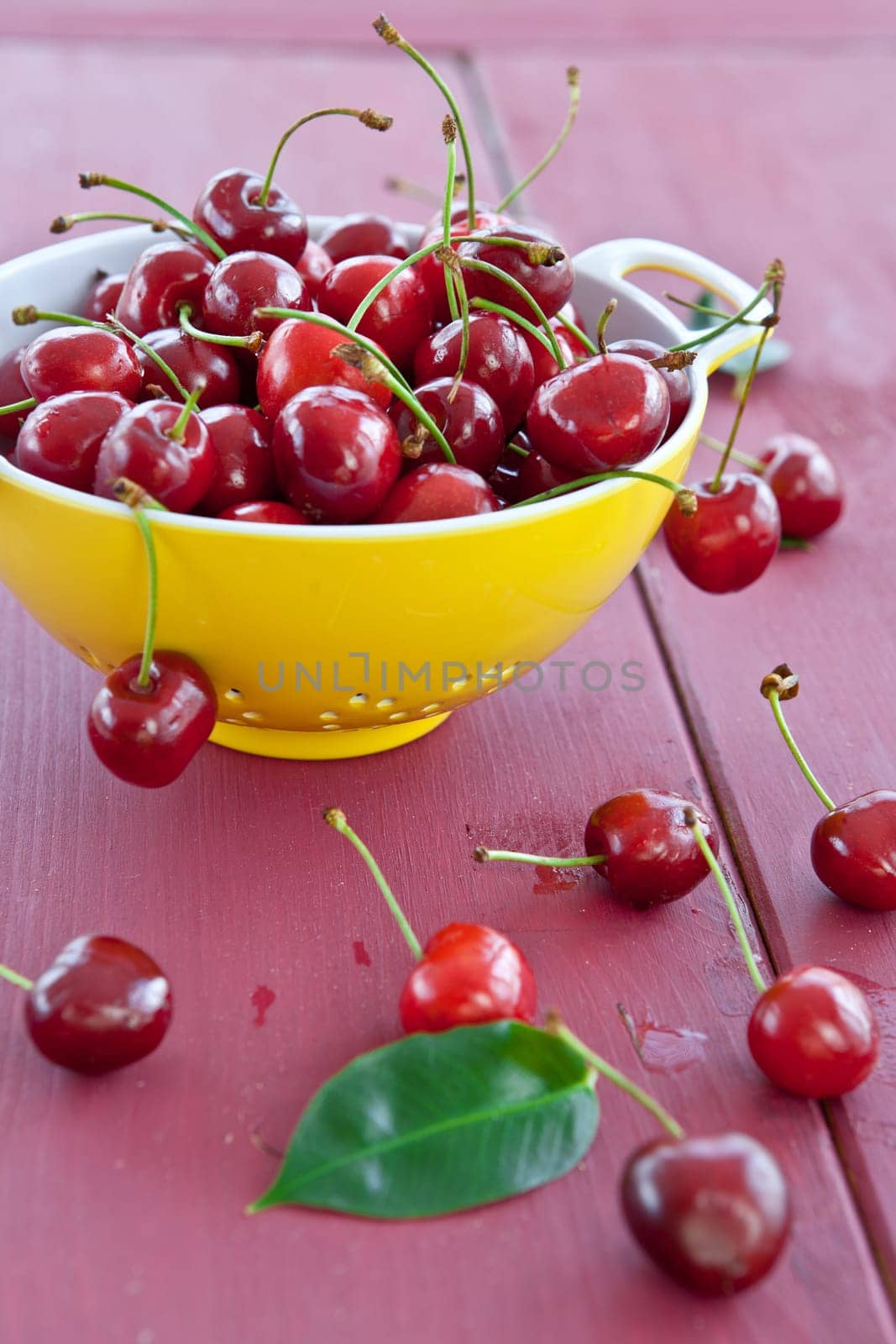Fresh cherries in yellow sieve on dark red table