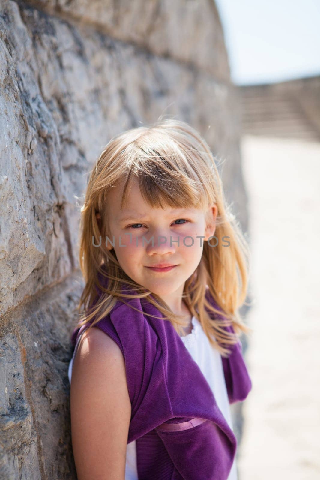 Closeup portrait of cute young girl leaning against brick wall at beach