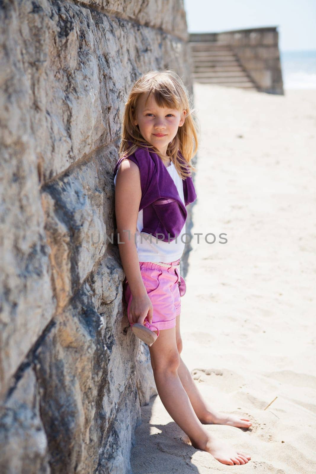 Portrait of cute young girl leaning against brick wall at beach