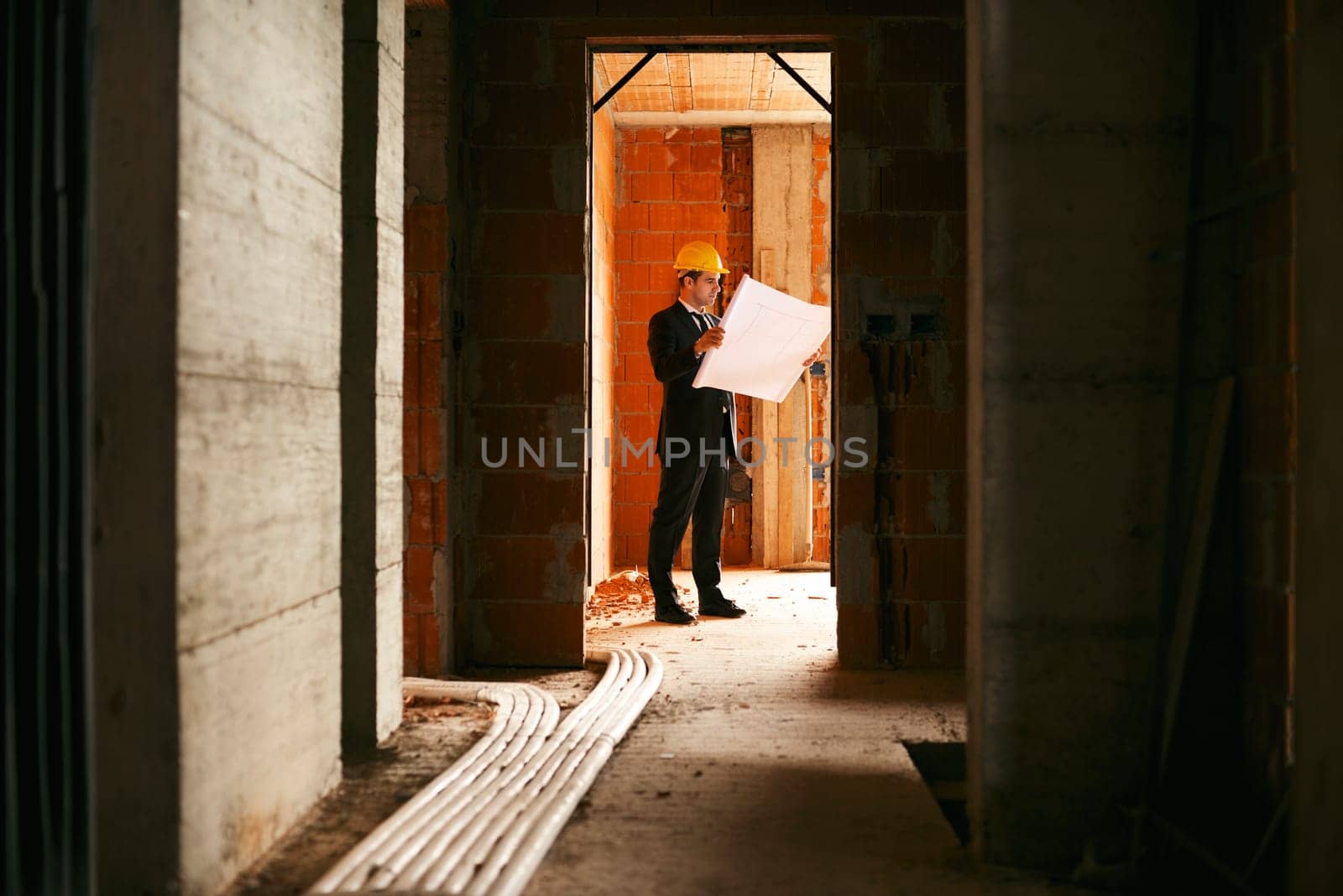 Engineer at work in construction site, standing in apartment building and looking at blueprints and plans