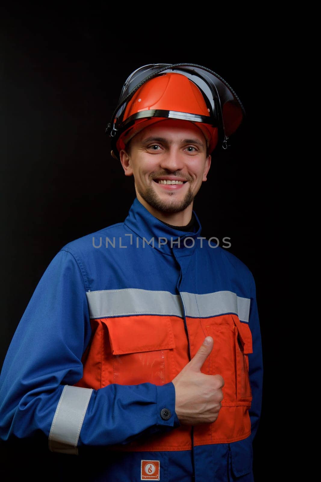 The worker in overalls and a helmet on a black background