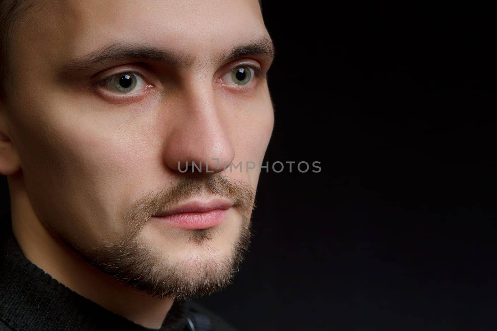 face of the young unshaven man in a black background