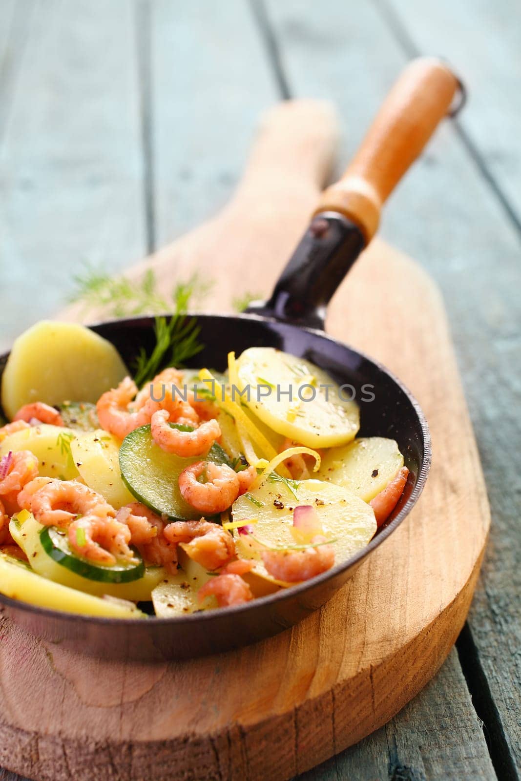 Prawns, zucchini and potato pan fried and served in the skillet on a wooden board for a healthy, fresh seafood meal