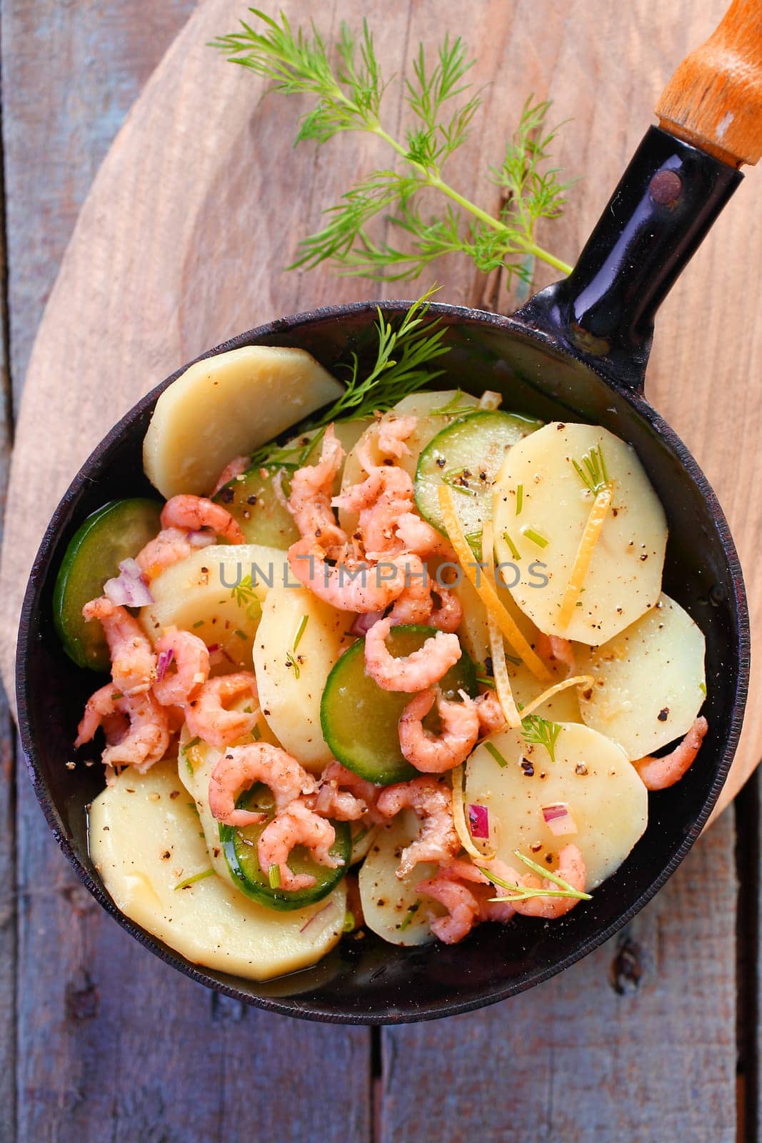 Delicious gourmet meal of prawns pan fried with potato and zucchini garnished with herbs and served in a metal skillet