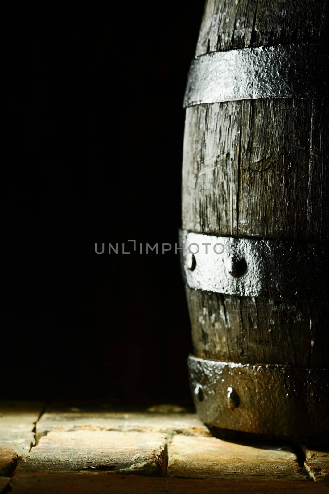 Old oak barrel standing upright on flagstones or old bricks with a dark background and copyspace conceptual of the aging and storing of wine, brandy or beer