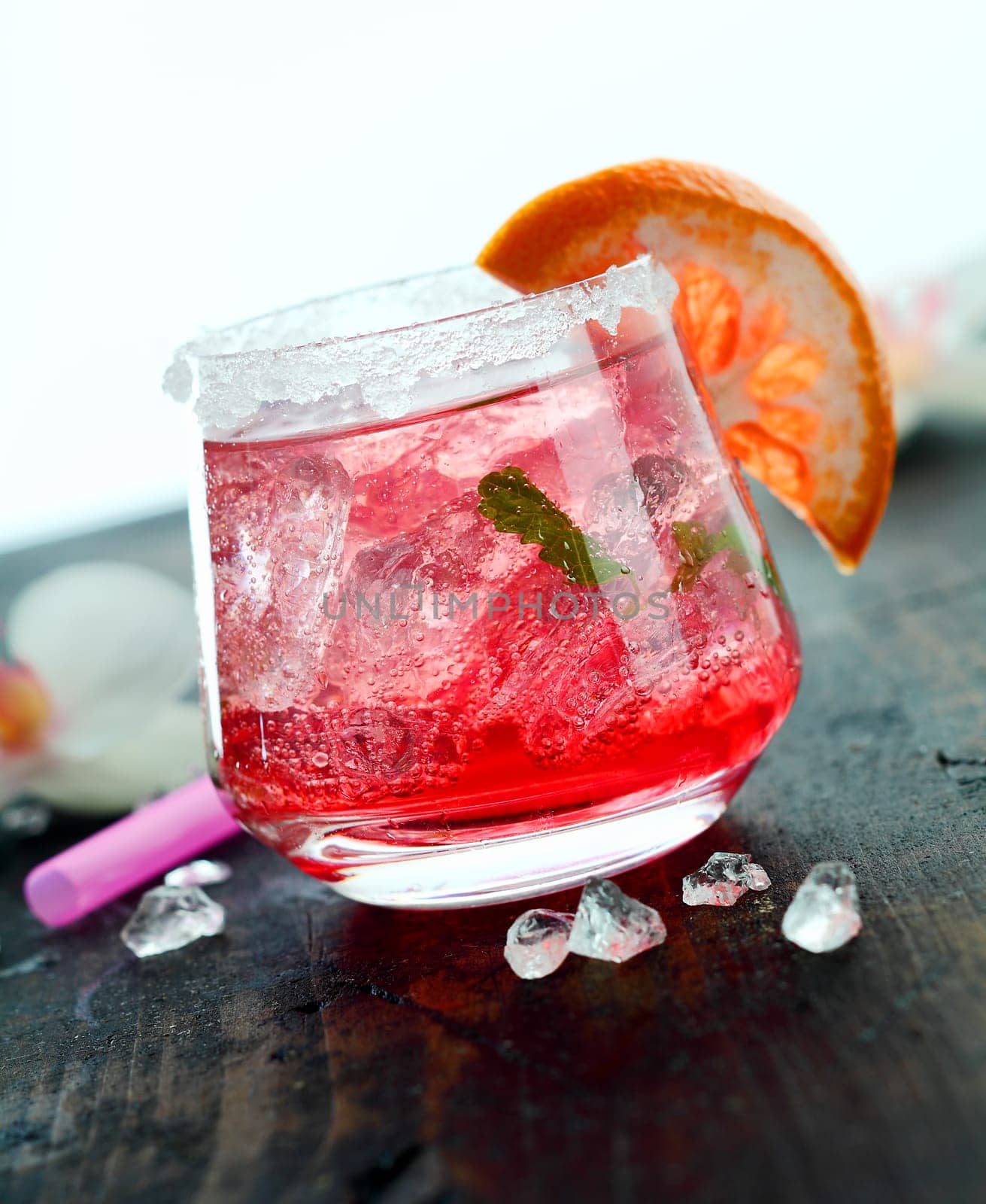 Ice cold daiquiri cocktail served in a tumbler garnished with orange on a wooden bar counter