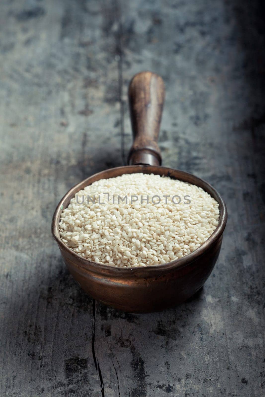 High-angle view of an old copper ladle filled with raw sesame over an old grungy grey wood table