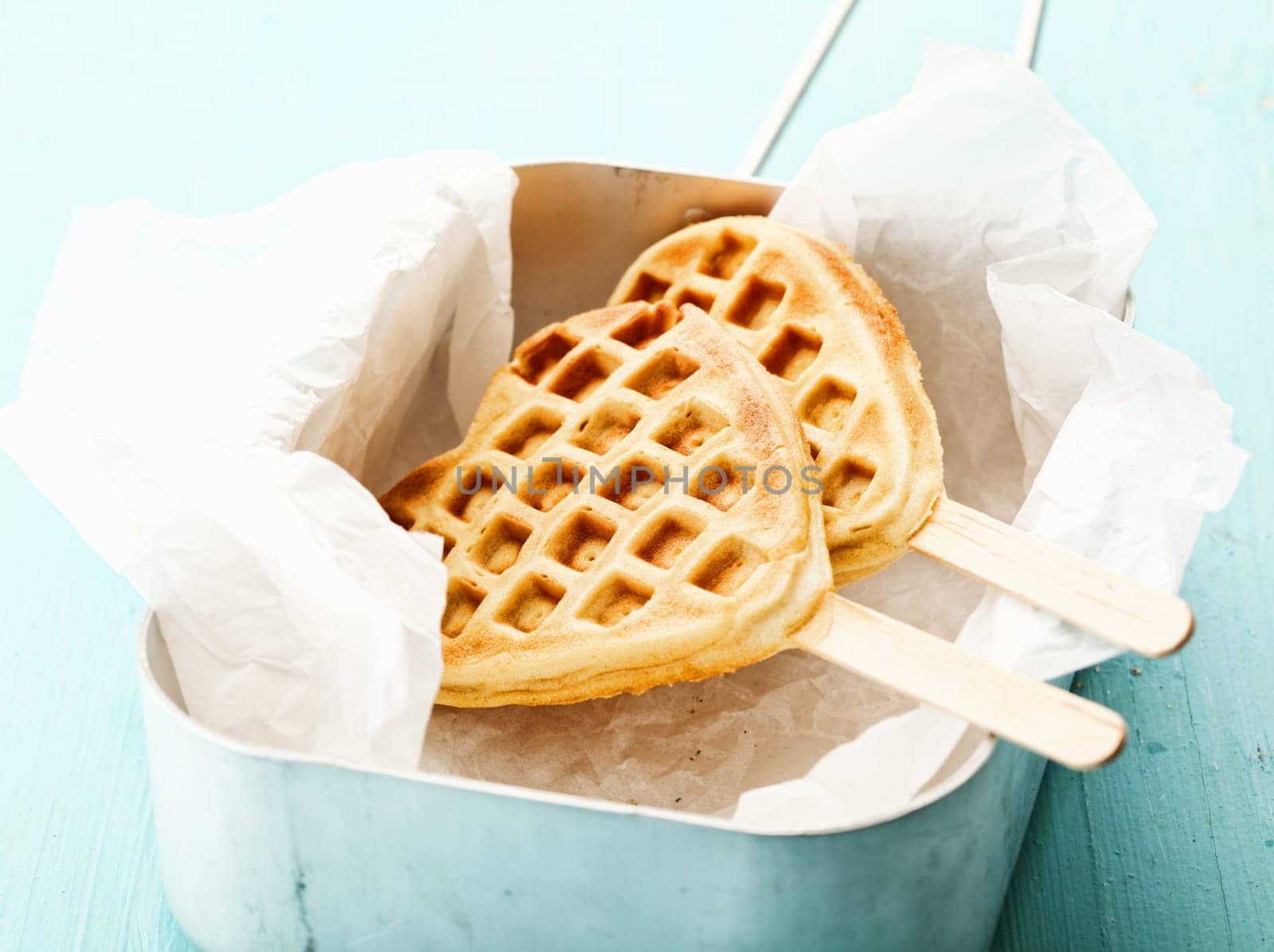 Fun crisp golden heart-shaped waffle popsicle with the traditional honeycomb pattern and a wooden stick on crumpled paper in a tin