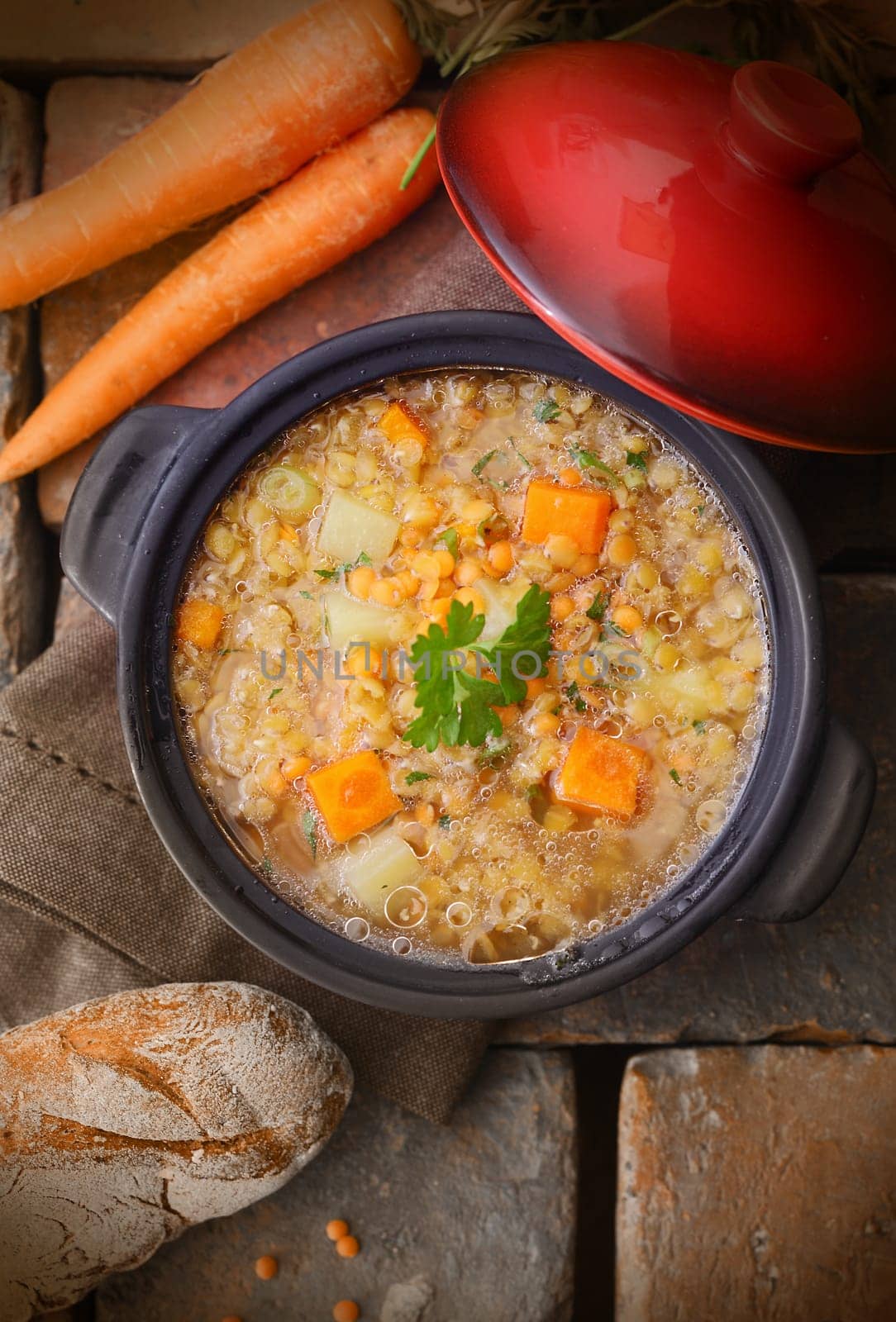 Top view of a warm and delicious freshly made pot of soup with raw carrots, chickpeas and a loaf of rustic bread
