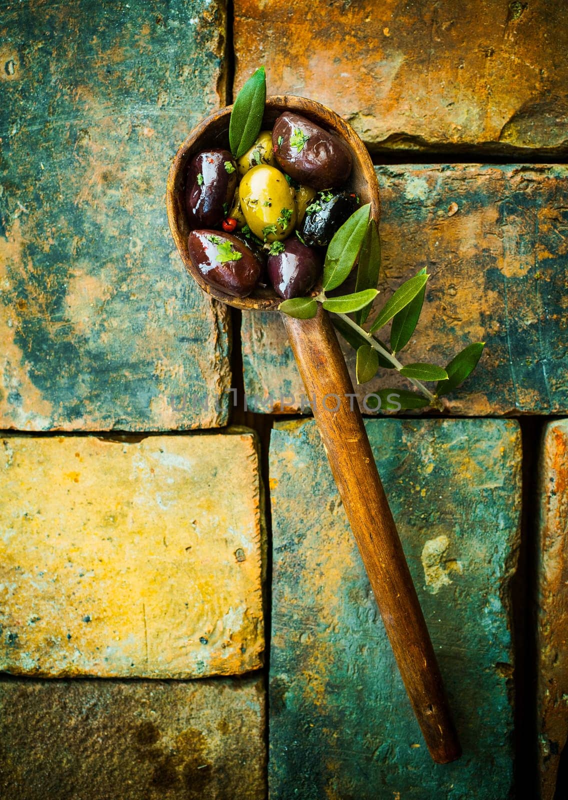 Overhead view of green and black olives in an old wooden ladle with leaves lying on grunge bricks with remnants of old paint with copyspace